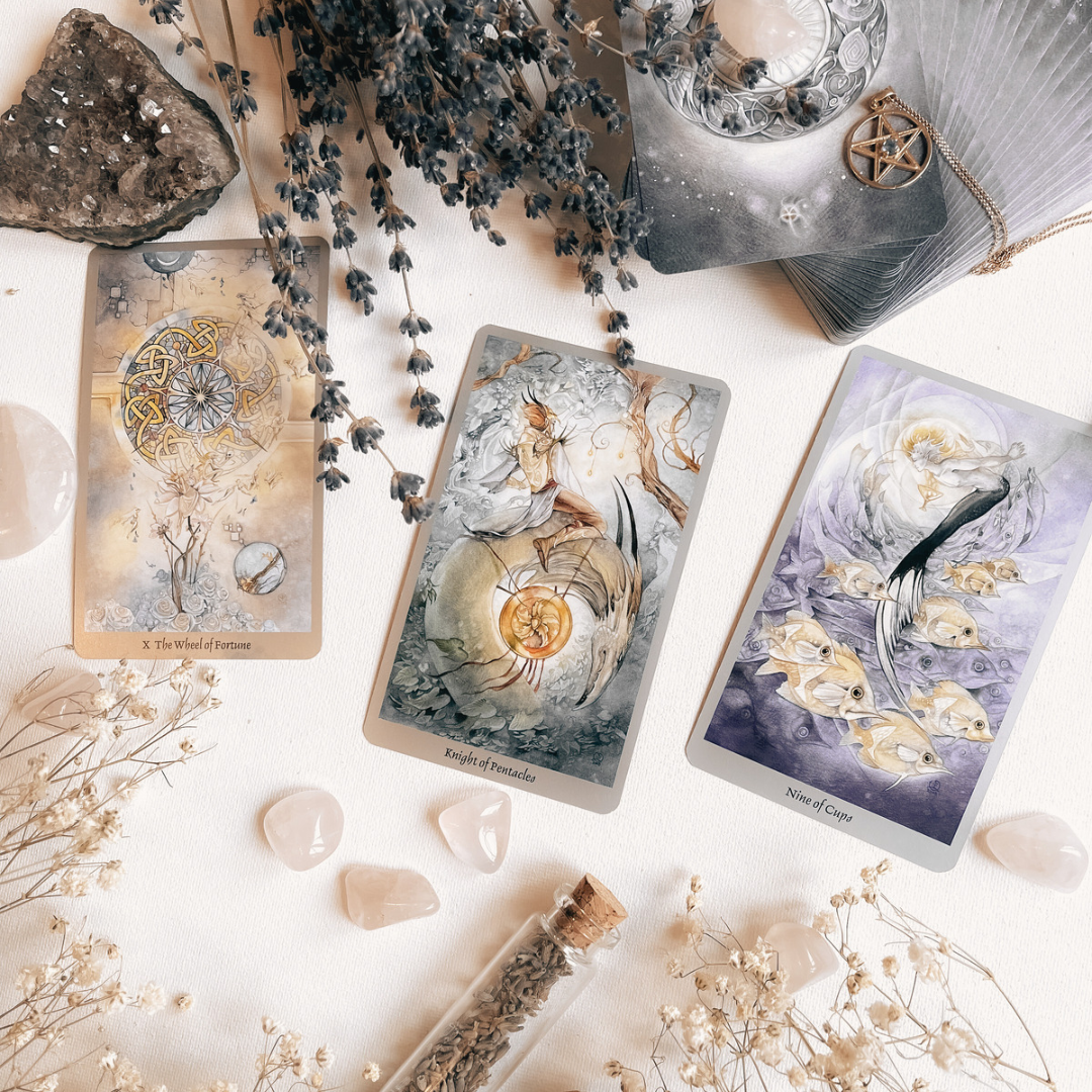 A simple 3 card tarot spread overlooked by a raw amethyst geode and a scattering of crystals and flowers