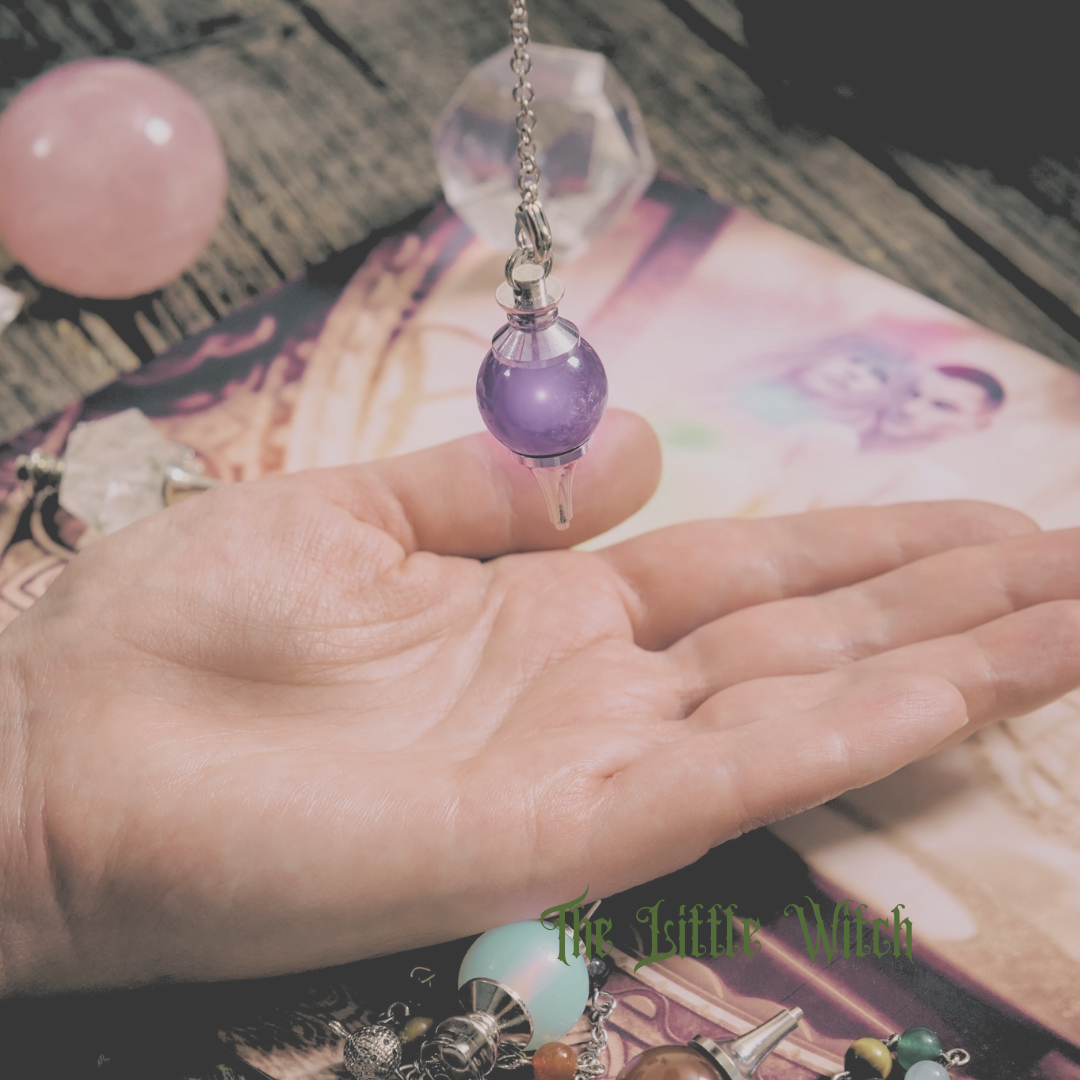 A hand lies flat on a table with an amethyst pendulum suspended above it