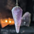 Amethyst crystal pendulum against a dark background with candle light 