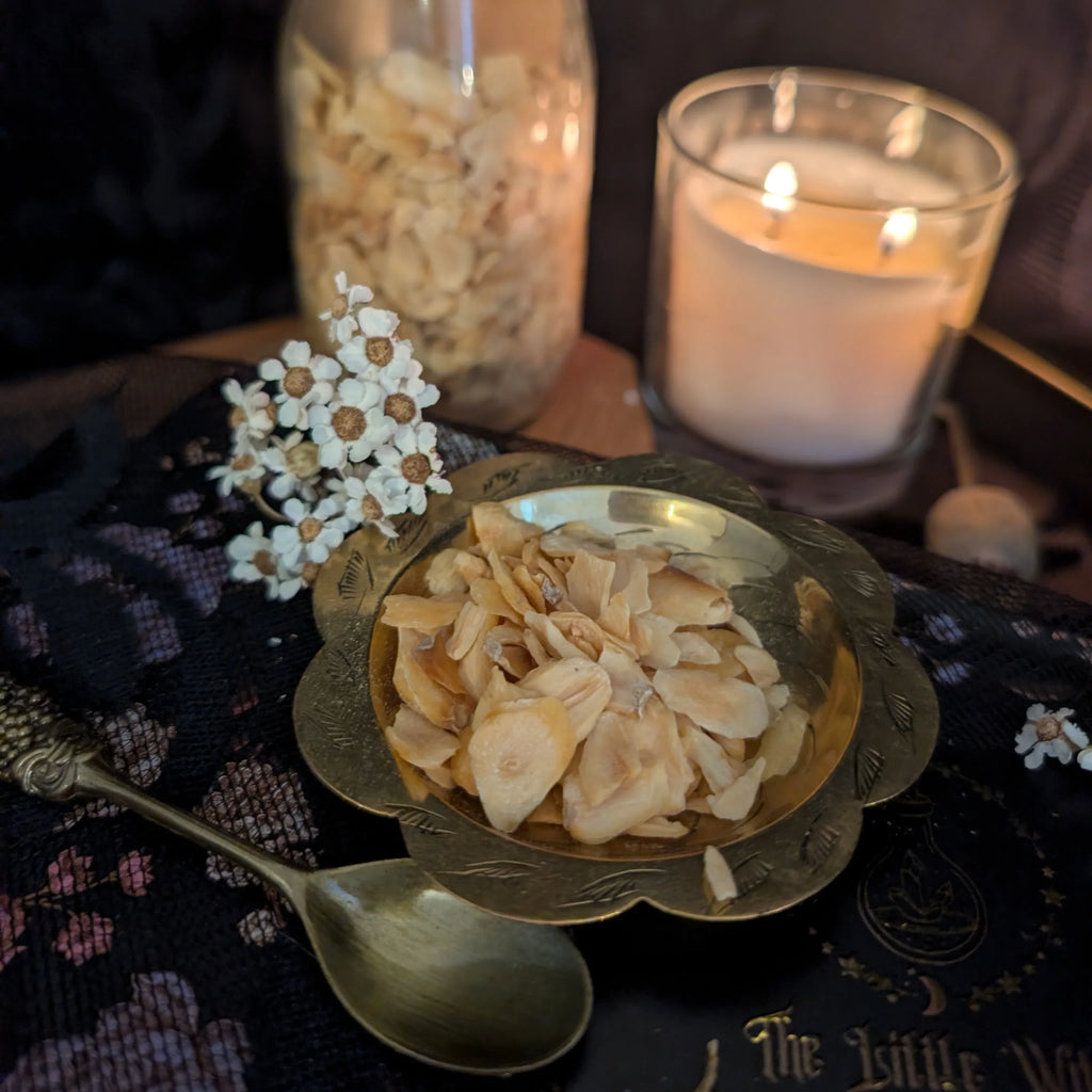Dried  garlic in a gold bowl with a lit candle and spoon on a dark surface