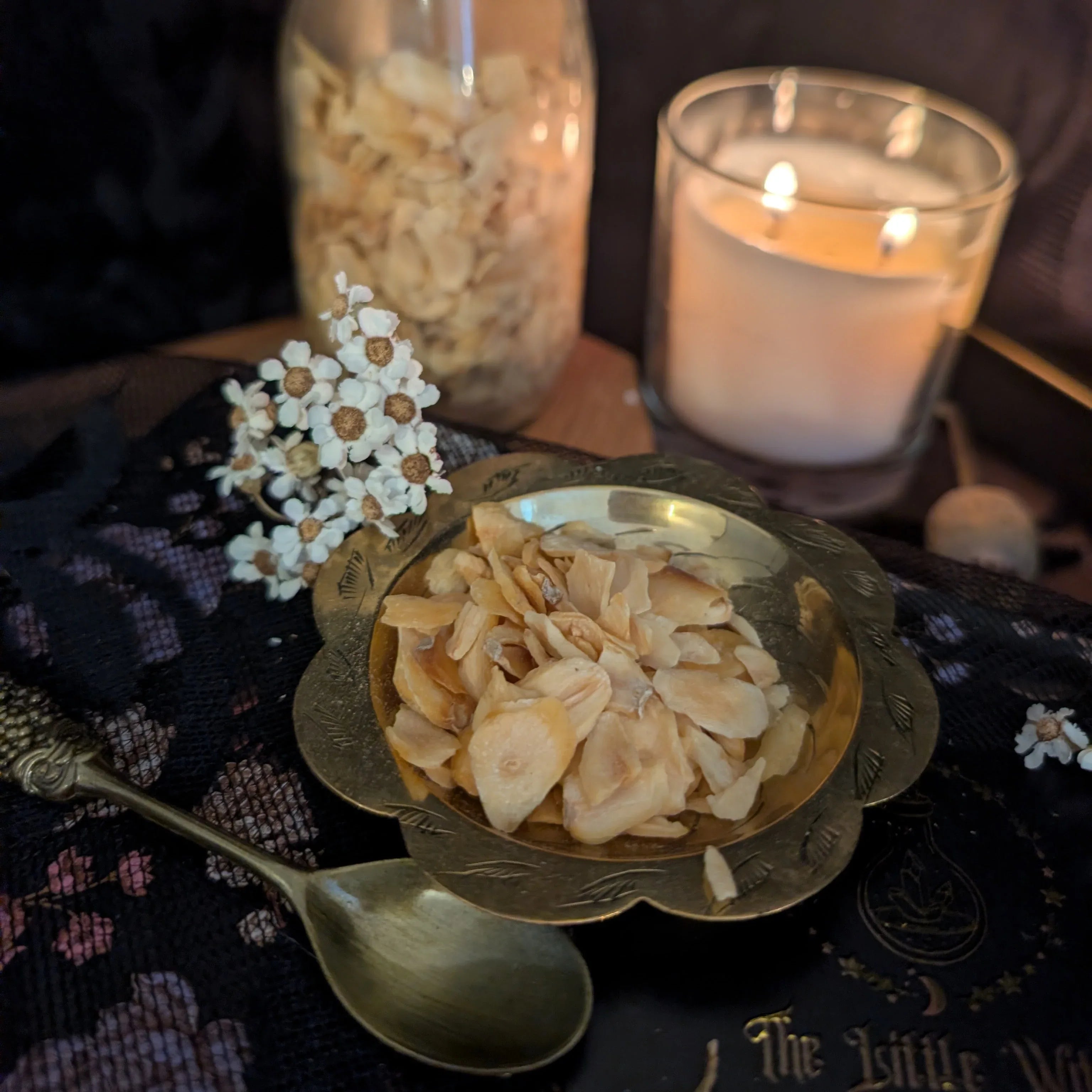 Dried  garlic in a gold bowl with a lit candle and spoon on a dark surface