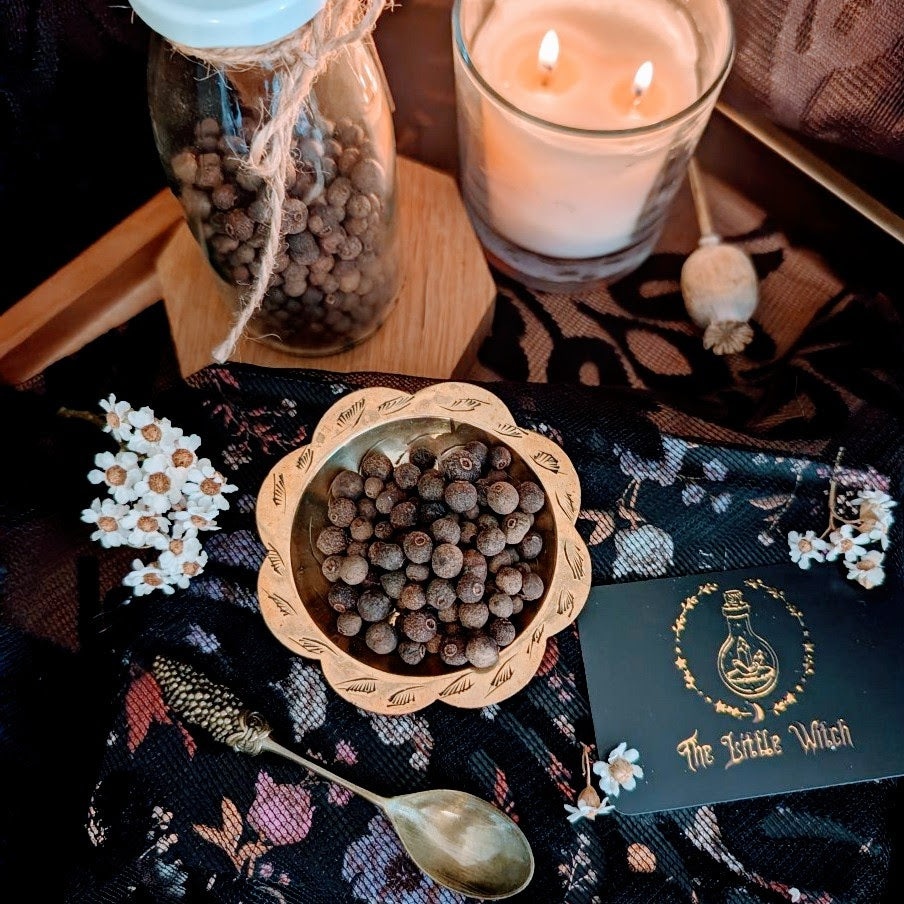 Allspices in a gold bowl with a lit candle and decorative card on a dark fabric background