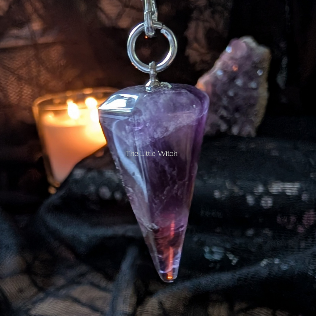 Amethyst pendulum on a dark fabric background with a candle