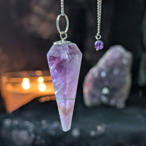 Amethyst crystal pendulum on a dark background with candles
