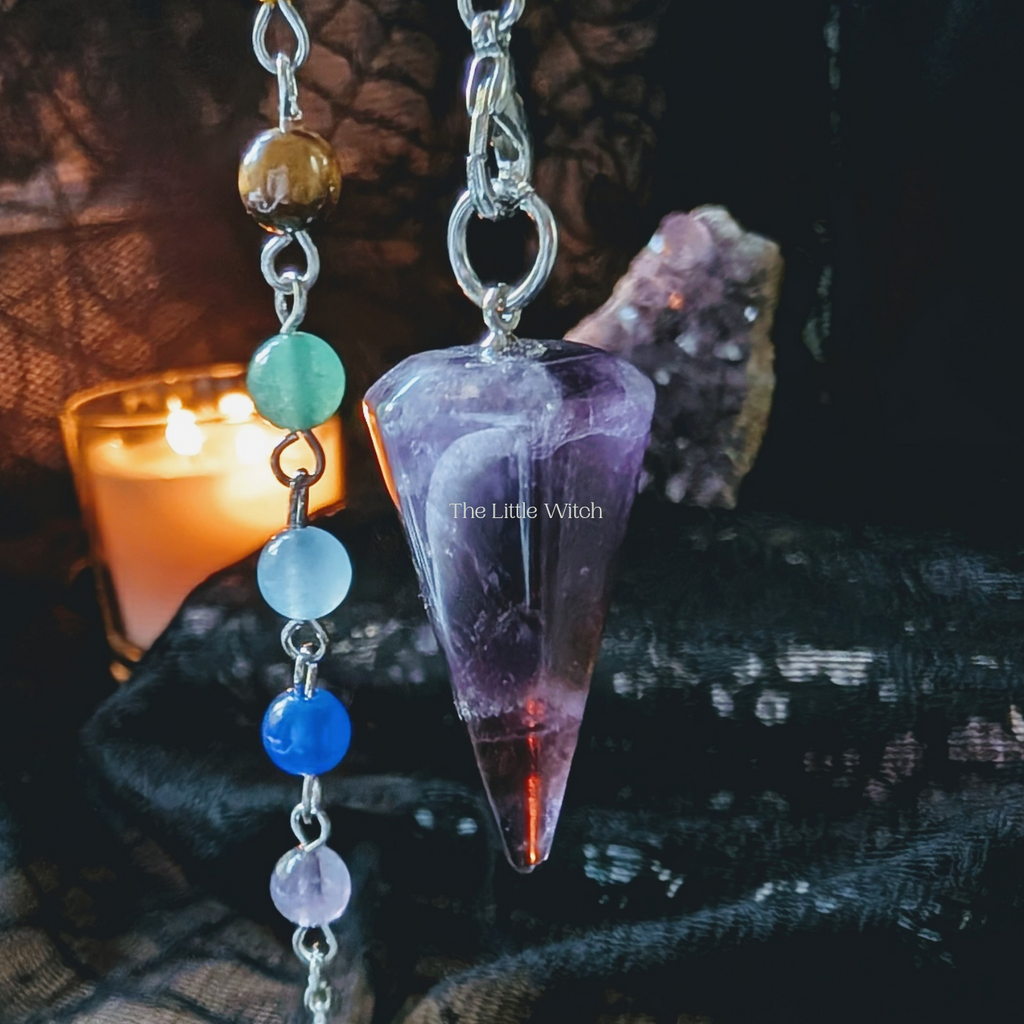 Amethyst crystal pendulum with colorful beads on a dark background with a candle.