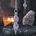 Purple crystal pendulum with silver accents on a dark background