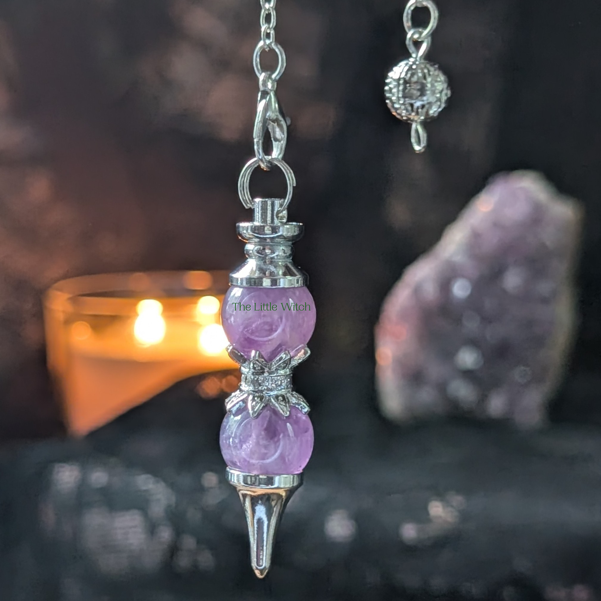 Purple crystal pendulum with silver accents on a dark background