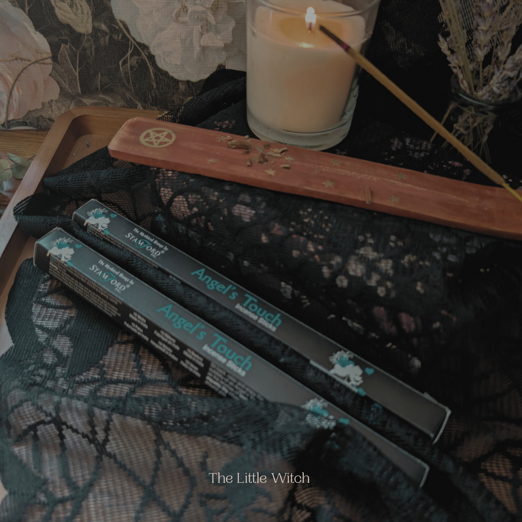Wands and packaging labeled 'Angel's Touch' on a dark, textured surface with a candle.