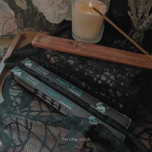 Wands and packaging labeled 'Angel's Touch' on a dark, textured surface with a candle.