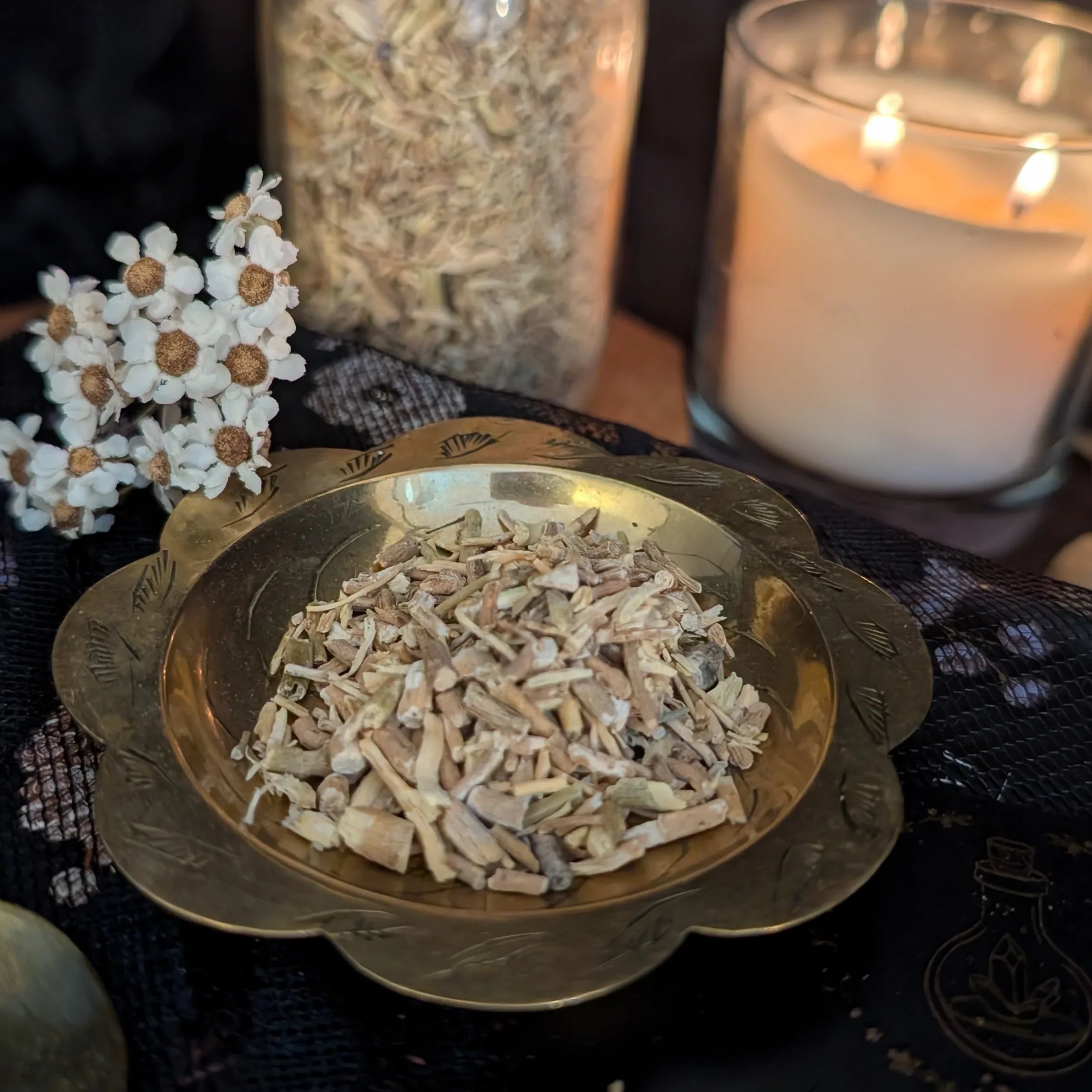 Herbal ingredients in a gold bowl with a candle and flowers in the background