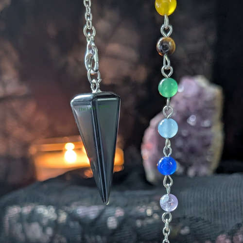 Black obsidian chakra pendulum with beads of crystals to represent each chakra, on a backdrop of black lace.