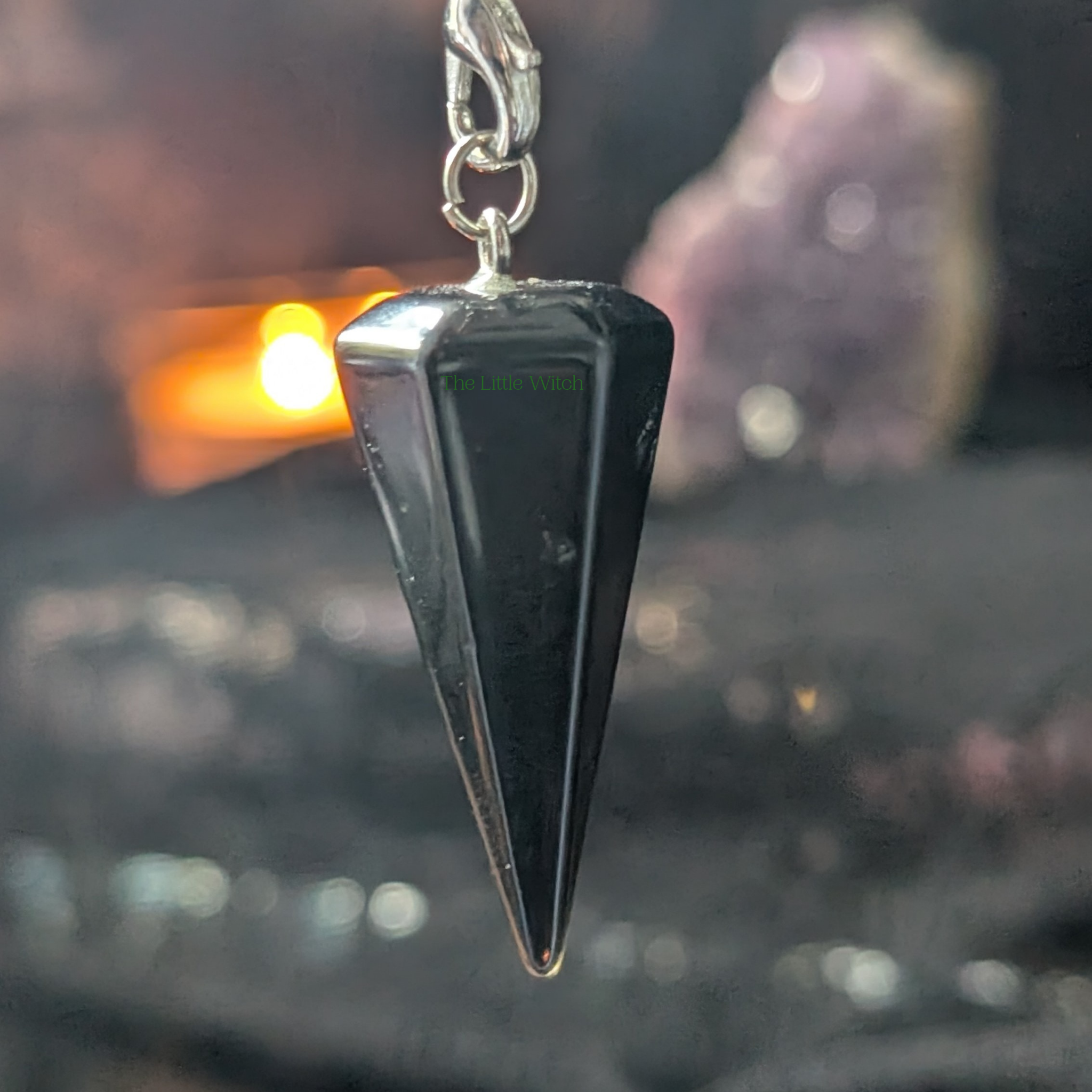 Black Obsidian Chakra Pendulum with black lace cloth backdrop. A softly lit candle and Amethyst geode are in the background.