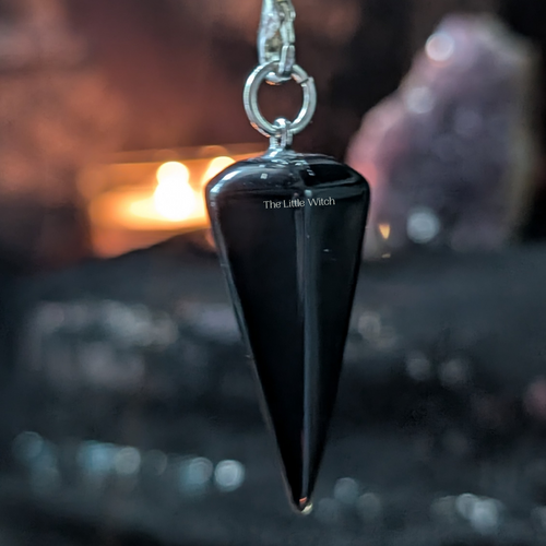 Black pendulum with chain on a dark background with blurred candle and crystal