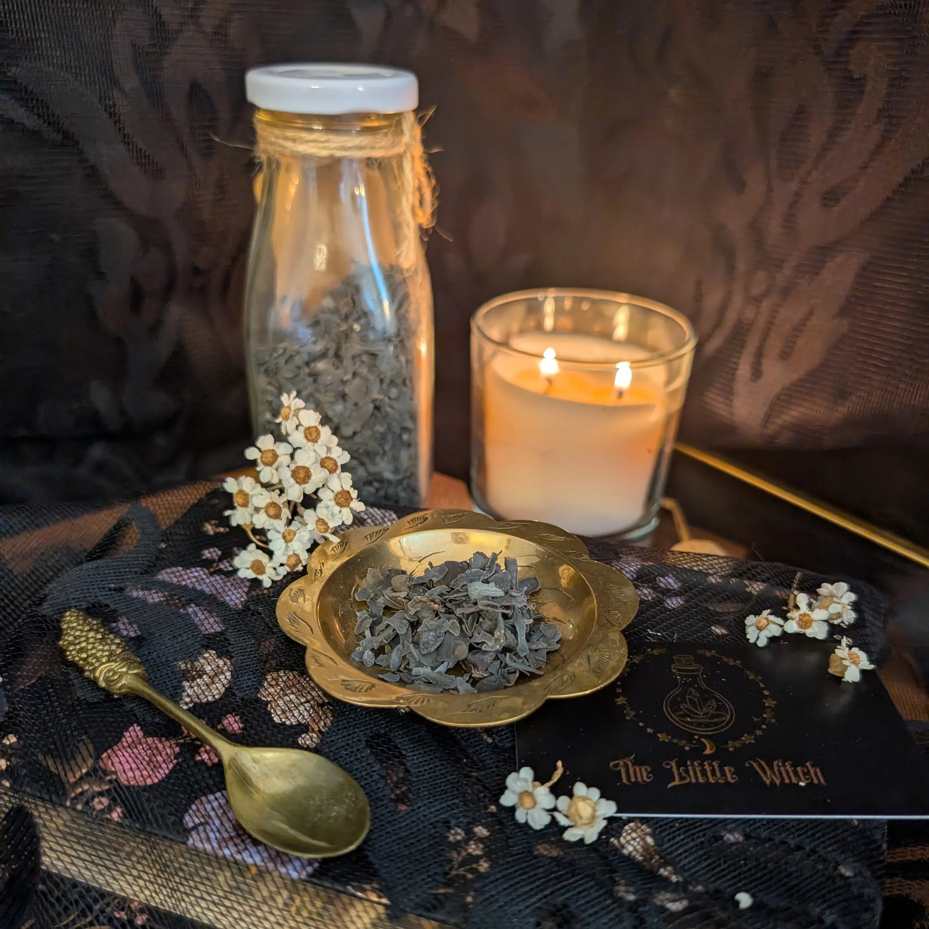 Spells and rituals items including a bottle, candle, and herbs on a dark fabric background.