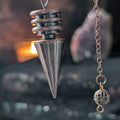 Metallic pendulum with chain against a black lace background