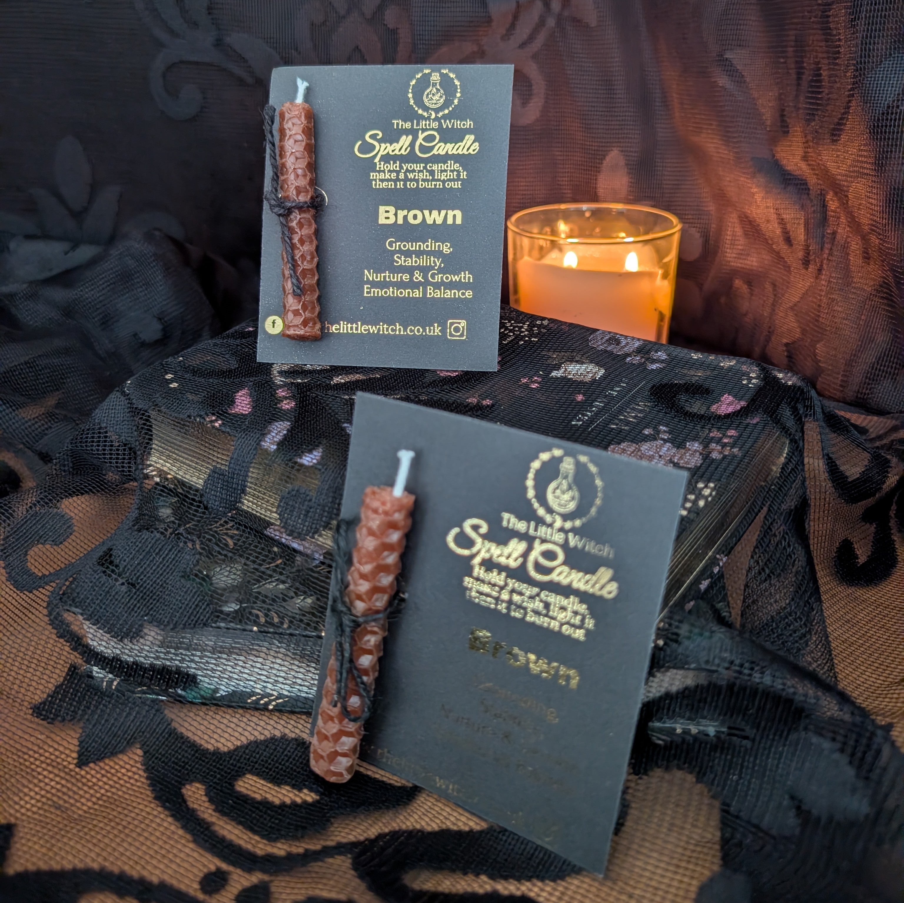 Two spell candles with packaging on a dark fabric background