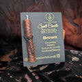 Brown beeswax candle mounted onto black card with gold 'The Little Witch' branding