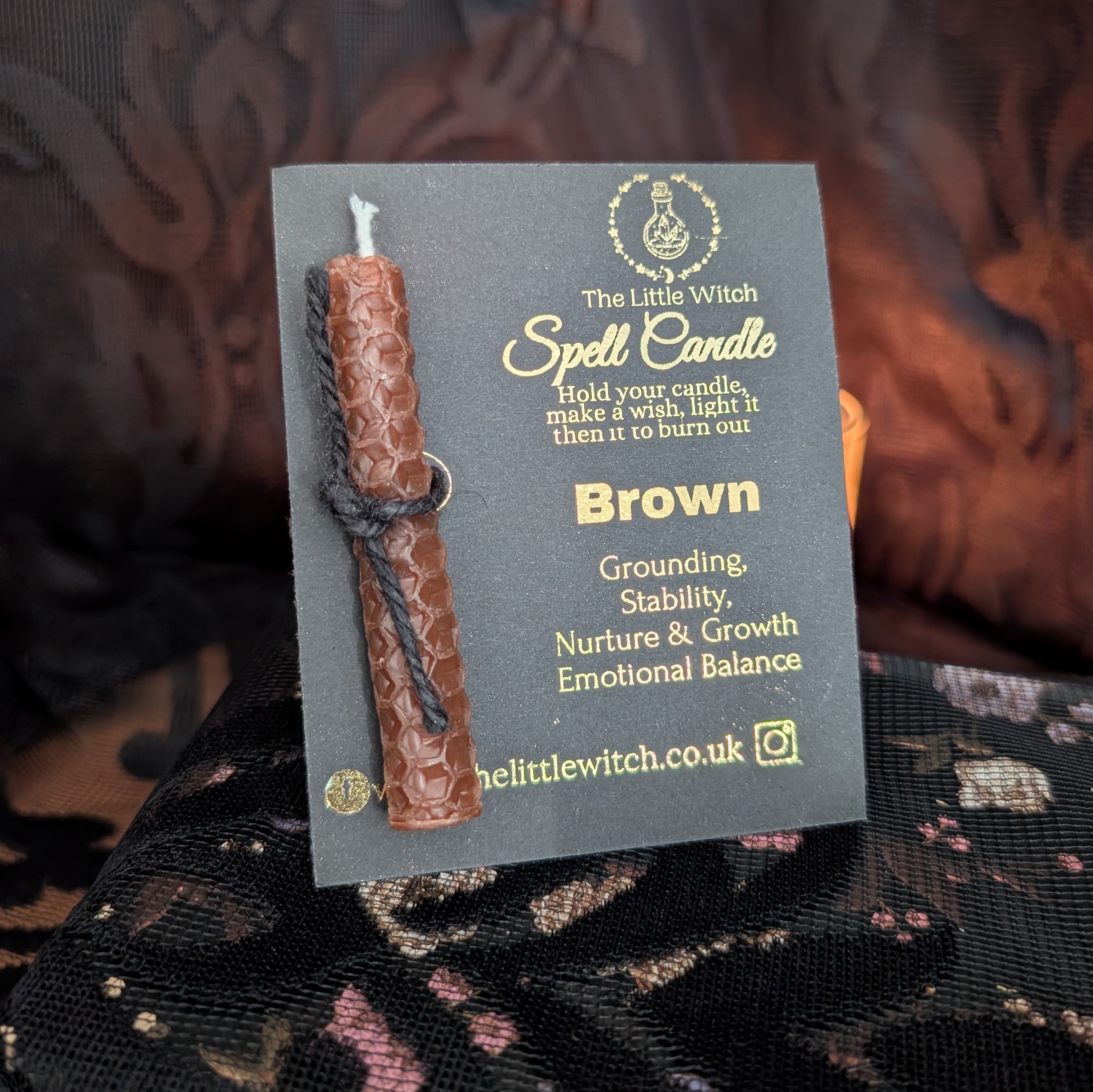 Brown beeswax candle mounted onto black card with gold 'The Little Witch' branding