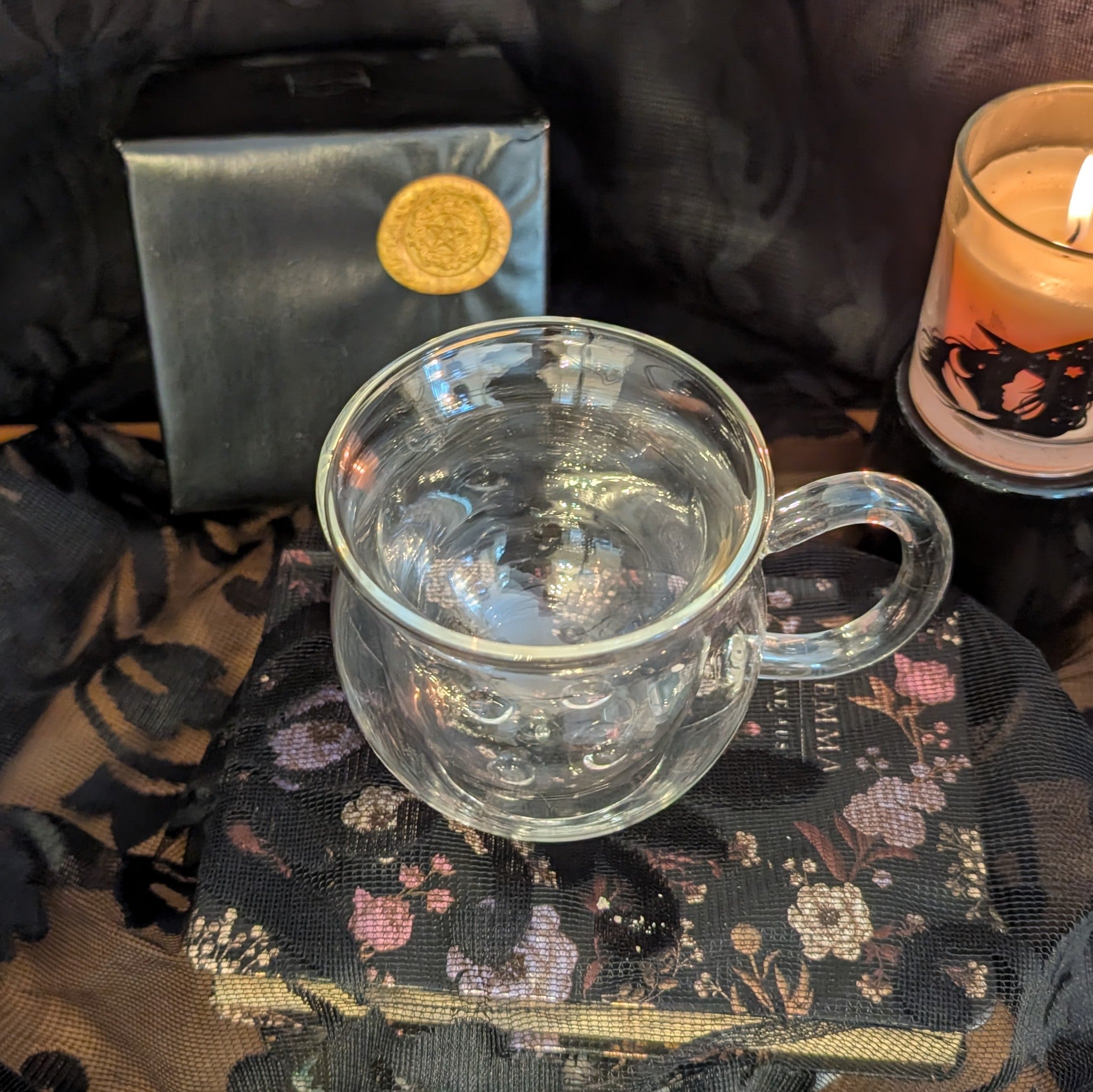 Clear glass mug on a decorative surface with a candle and box in the background