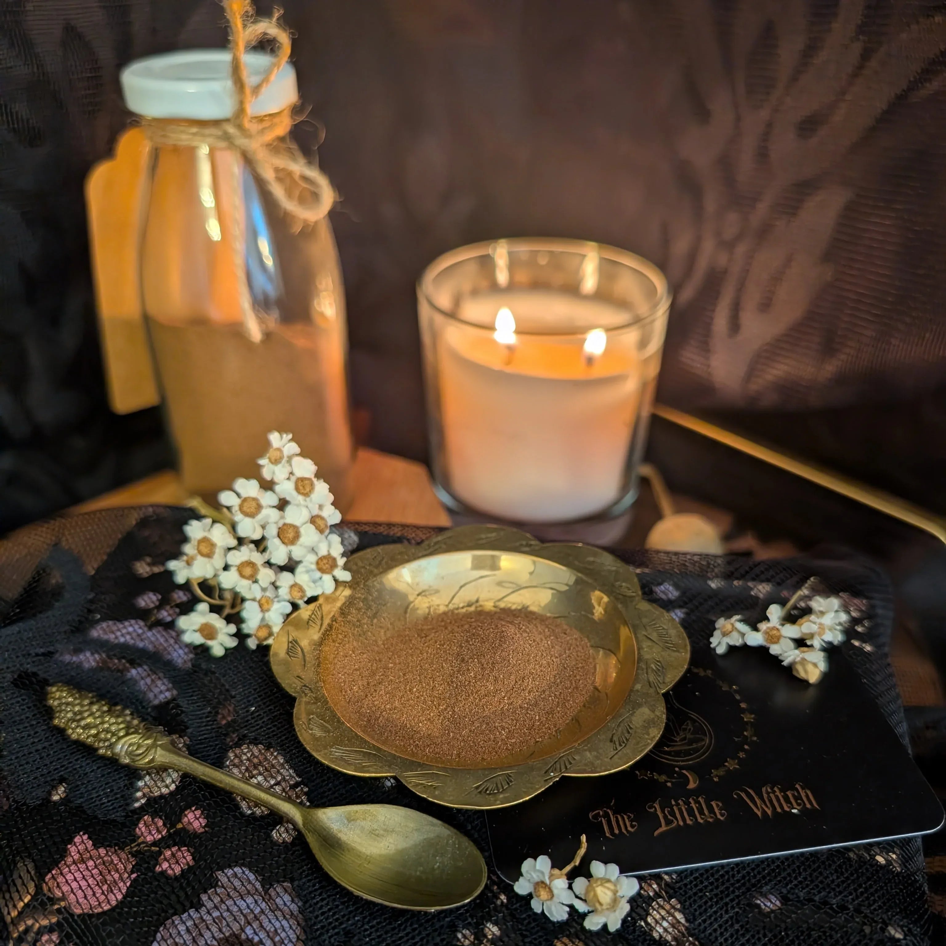 Spice jar, candle, and spoon on a black cloth with floral decorations