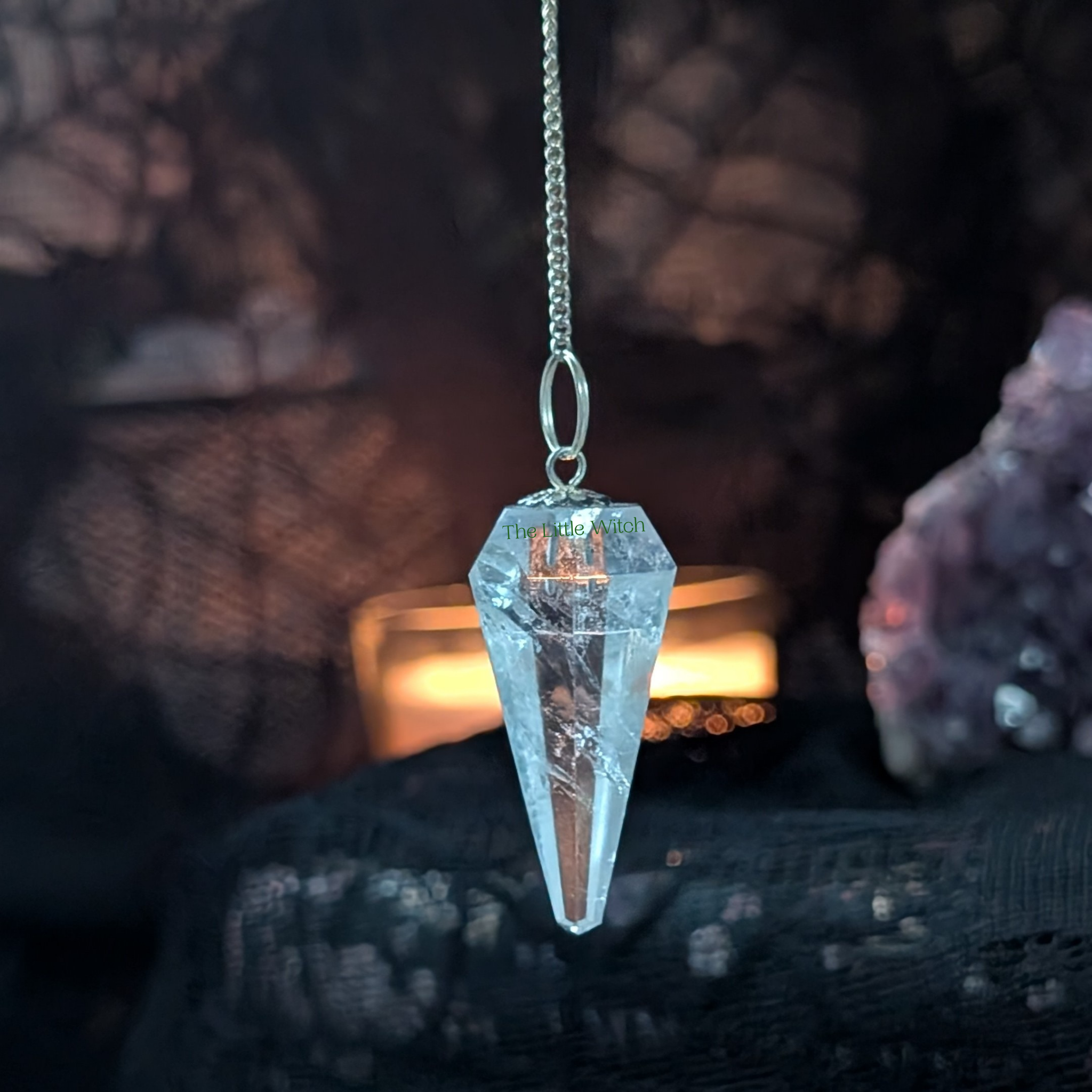 Crystal pendulum hanging against a dark background with rocks and a candle.