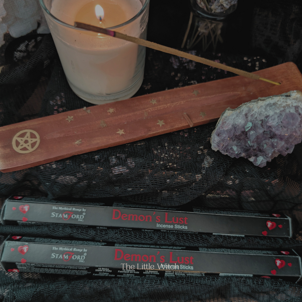 Incense sticks labeled 'Demon's Lust' with a candle and pentacle symbol on a dark surface.