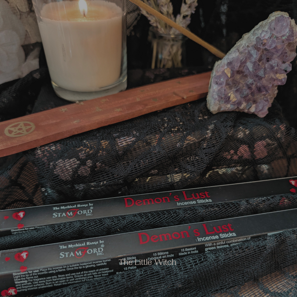 Incense sticks labeled 'Demon's Lust' on a black lace surface with a candle and crystal in the background.