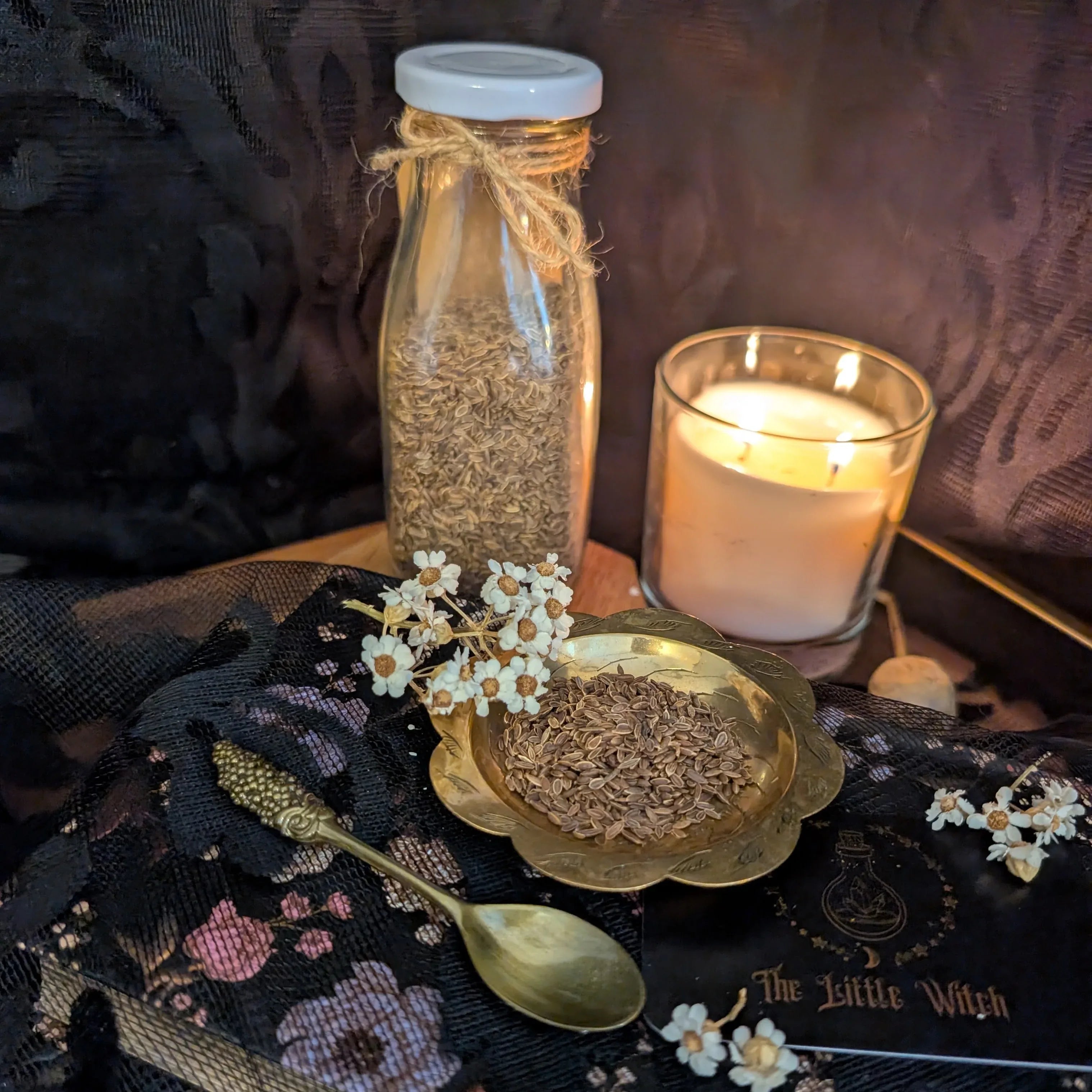 Dried Dill in a bottle and on a dish with a candle and spoon on a dark surface