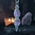 Purple crystal pendulum with silver accents on a dark background
