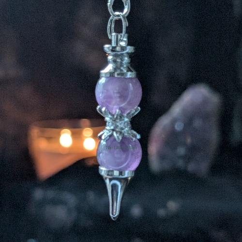 Purple crystal pendulum with silver accents on a dark background