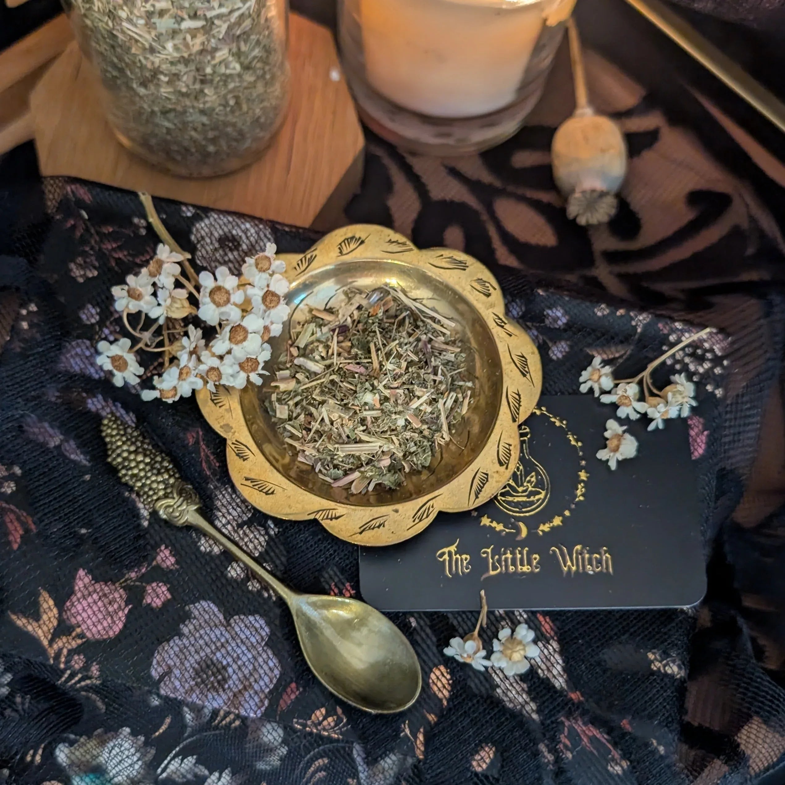 Marjoram in a gold bowl with 'The Little Witch' label on a dark floral fabric background.