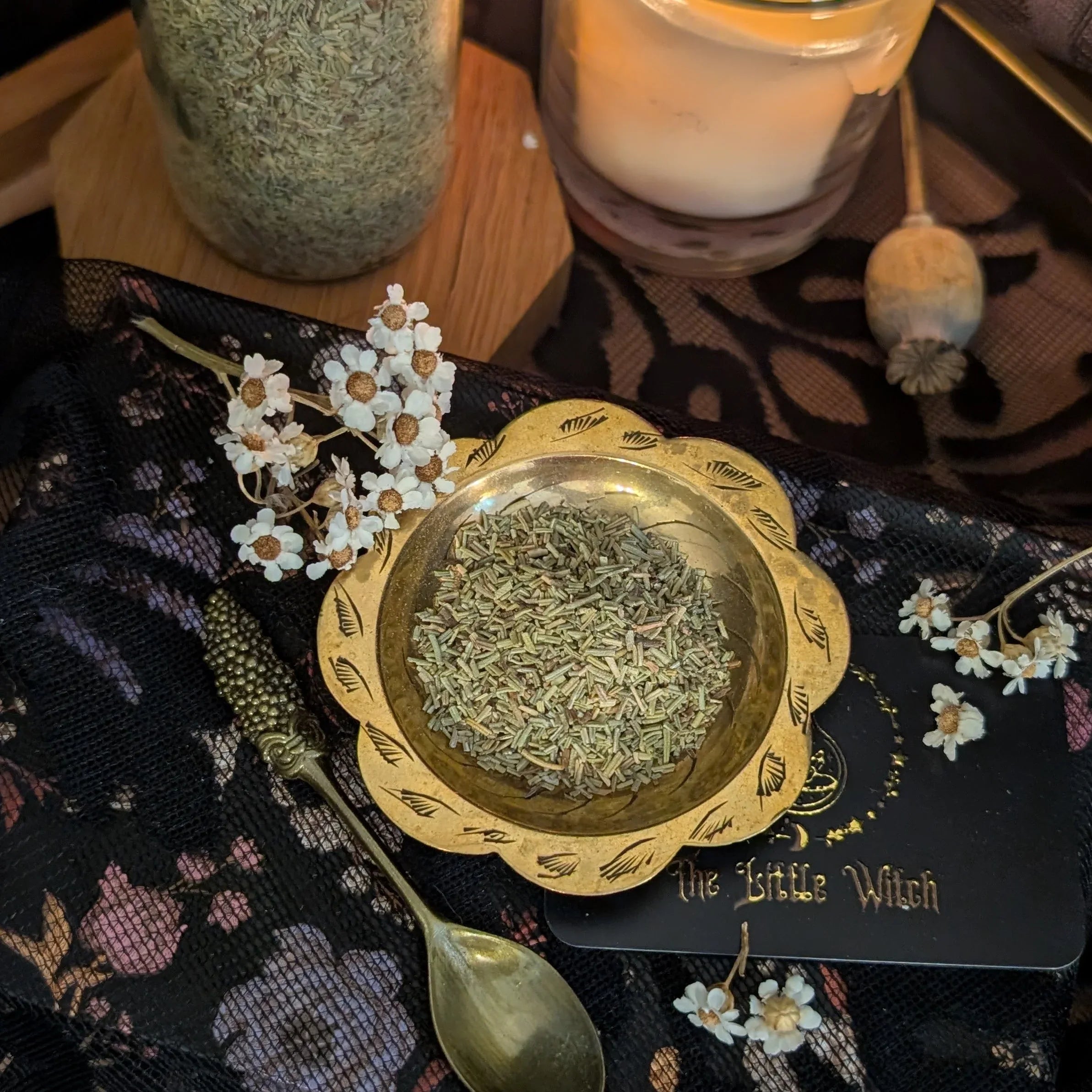 Dried Rosemary  in a gold dish on a decorative cloth with a candle and jar in the background.