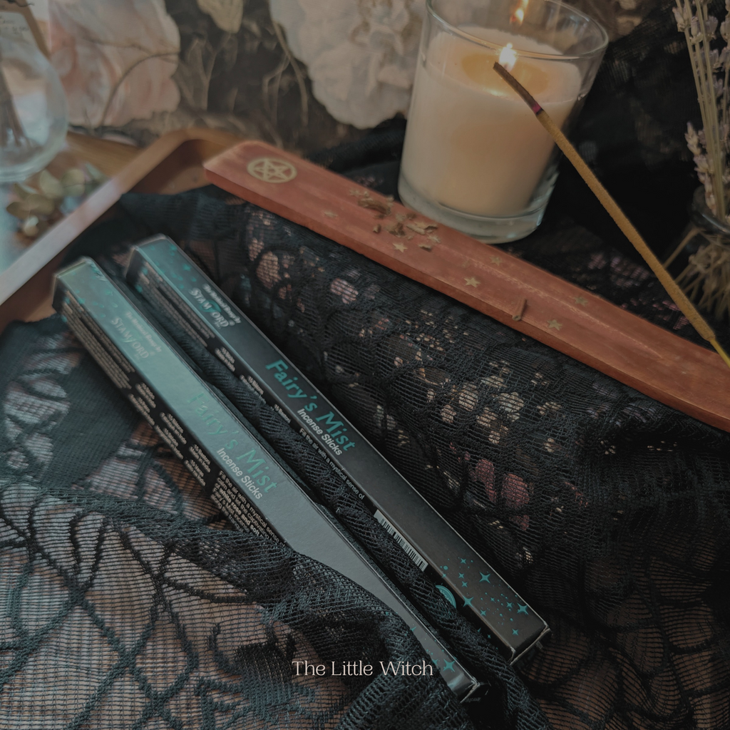 Two boxes of Fairy's Mist incense on a textured surface with a candle and decorative items in the background.