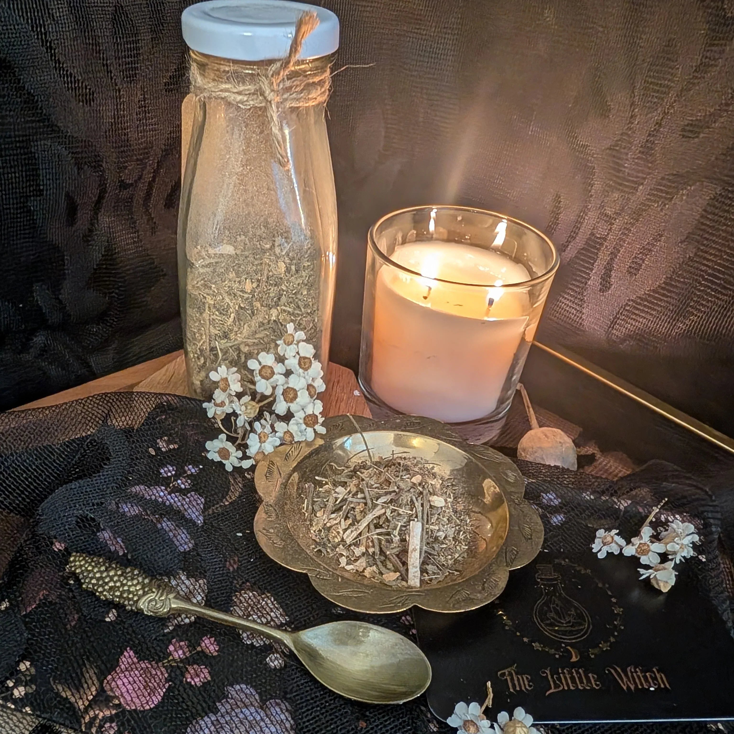 Decorative setup with a lit candle, bottle, spoon, and small dish on a dark surface.