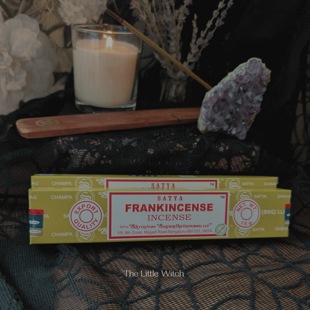 Frankincense incense box with a lit candle and crystals on a dark surface.