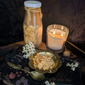 Decorative setup with a bottle, candle, and bowl on a dark surface with 'The Little Witch' book.