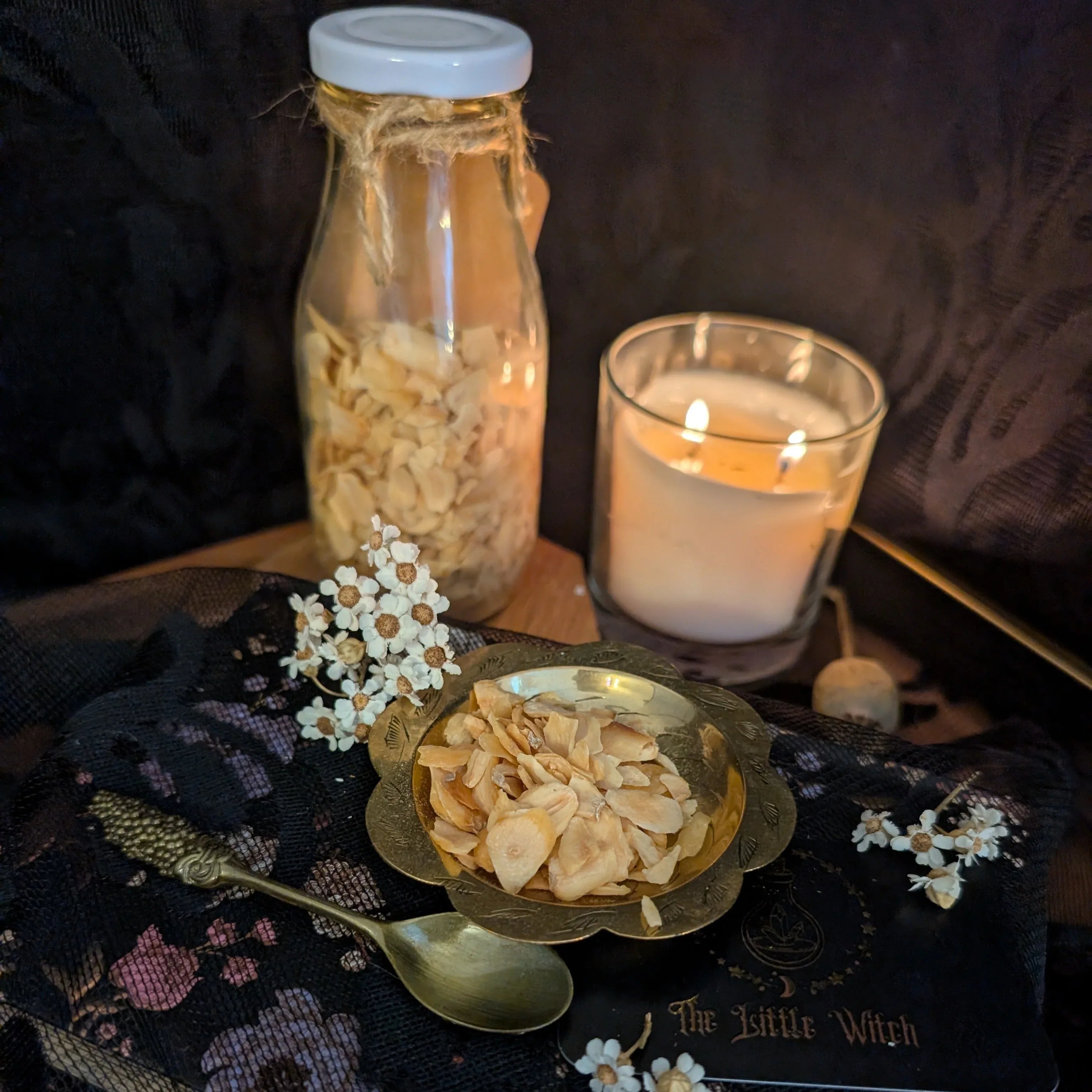 Decorative setup with a bottle, candle, and bowl on a dark surface with 'The Little Witch' book.