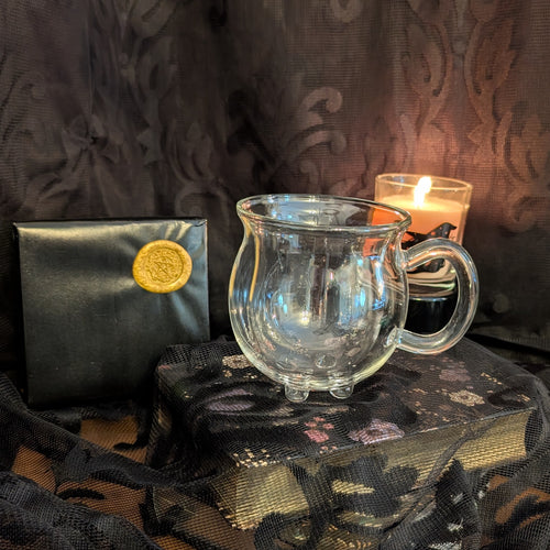 Clear glass mug on a dark surface with a candle and black pouch in the background.