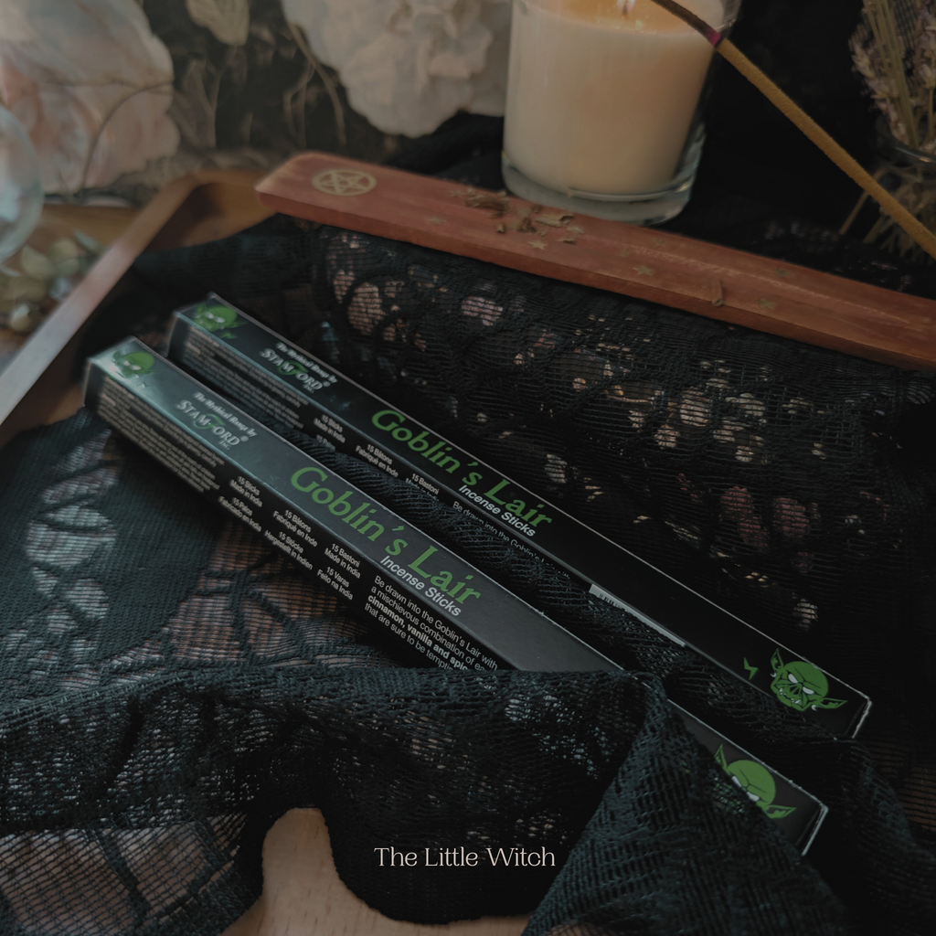 Incense sticks in packaging labeled 'Goblin's Lair' on a dark surface with a candle in the background.