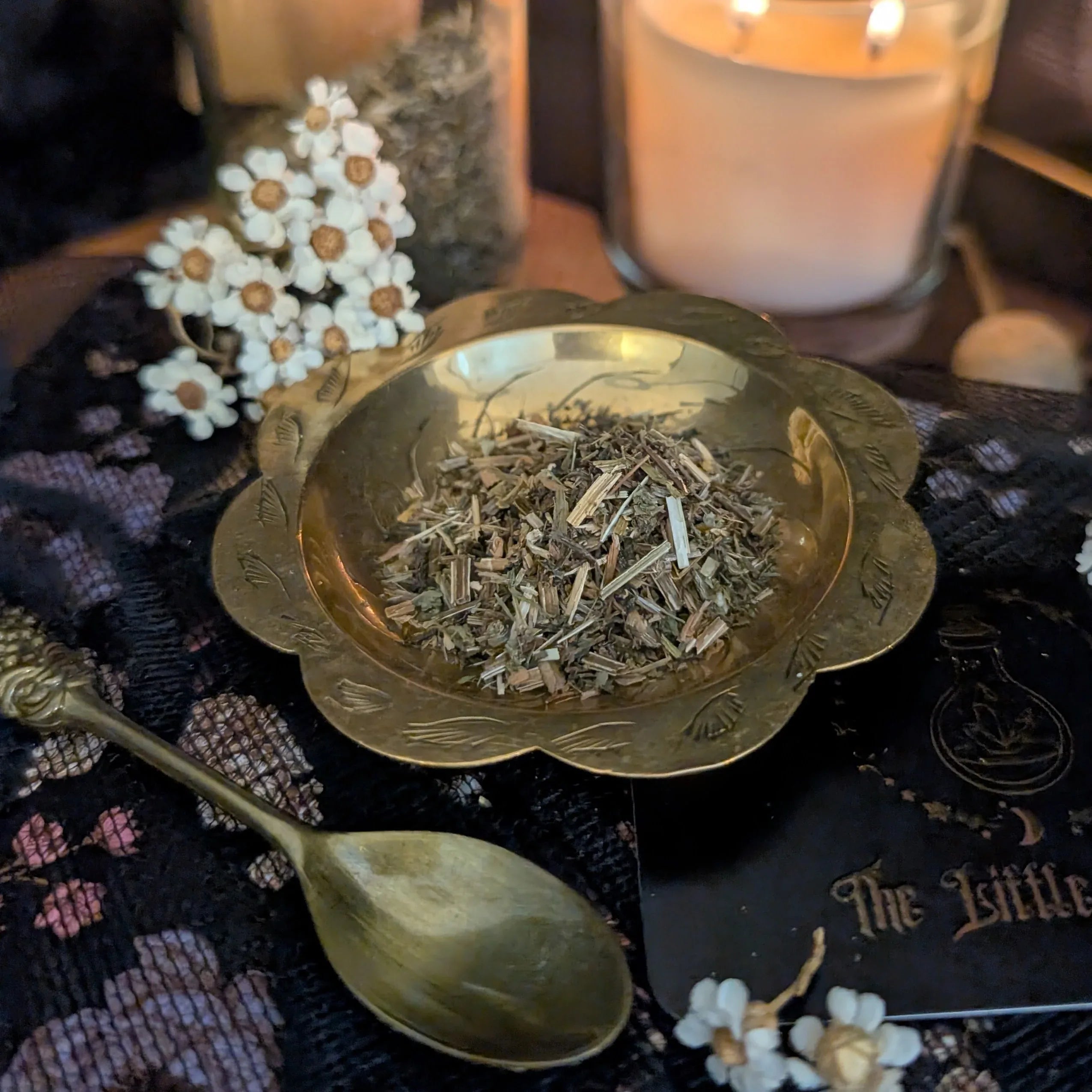 Dried Cleavers in a brass bowl with a candle and spoon on a patterned surface