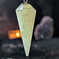 Green Aventurine faceted pendulum with dark background, softly lit candle and amethyst geode