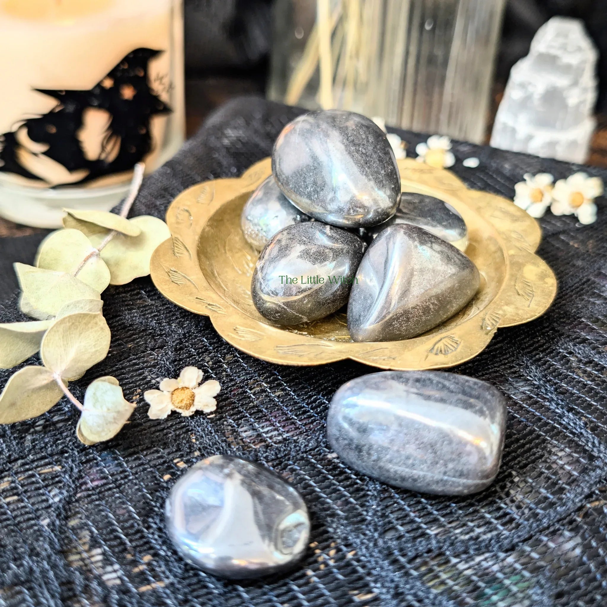 Decorative arrangement with Hematite stones in a gold dish on a textured surface.