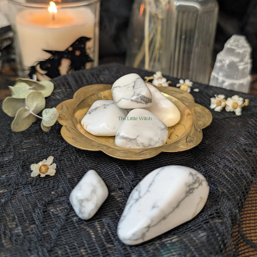 Howlite stones on a brass plate with decorative elements on a dark surface