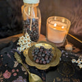 Decorative setup with juniper berries, candle, and bottle on a textured surface