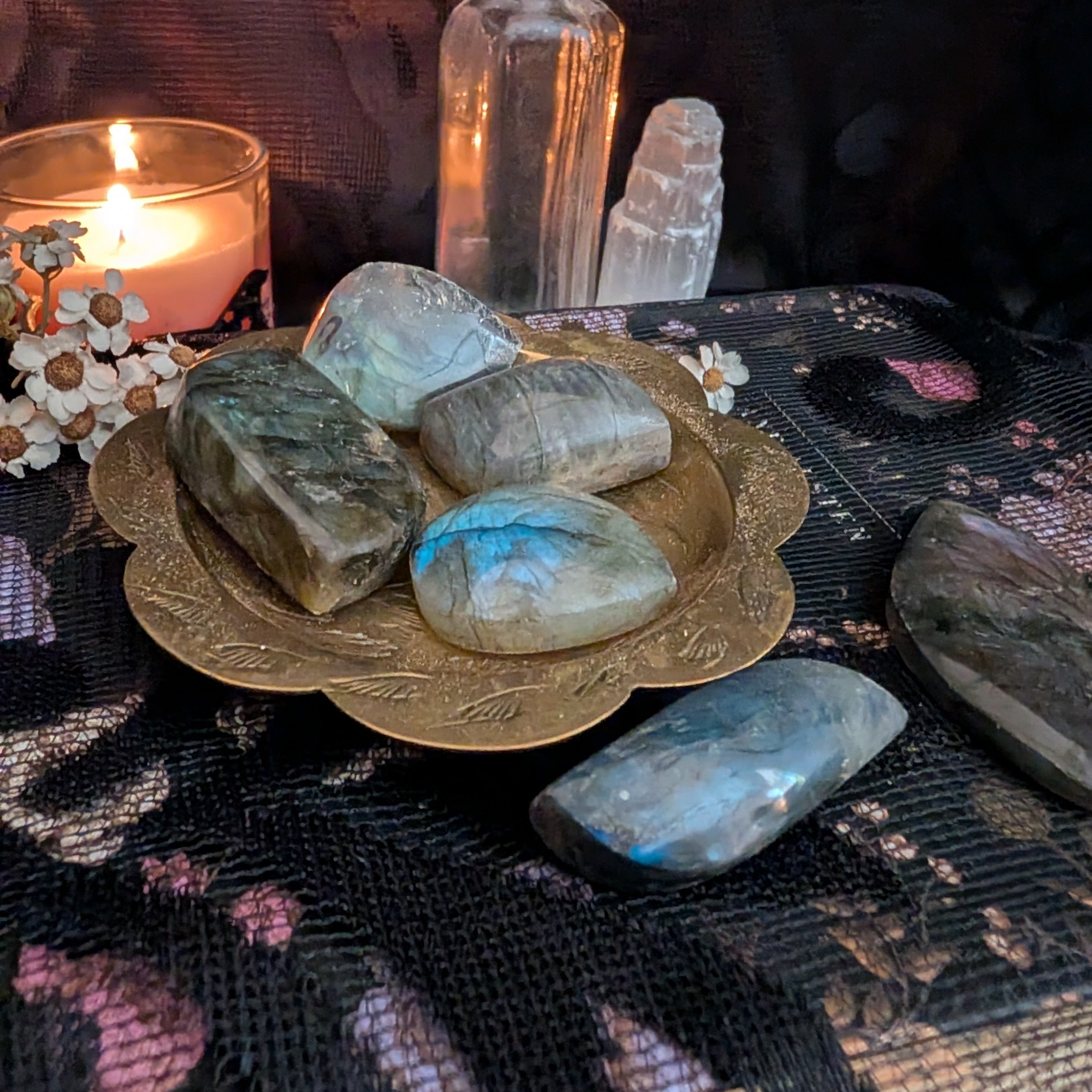 A collection of labradorite polished crystals in a gold dish surrounded by candlelight