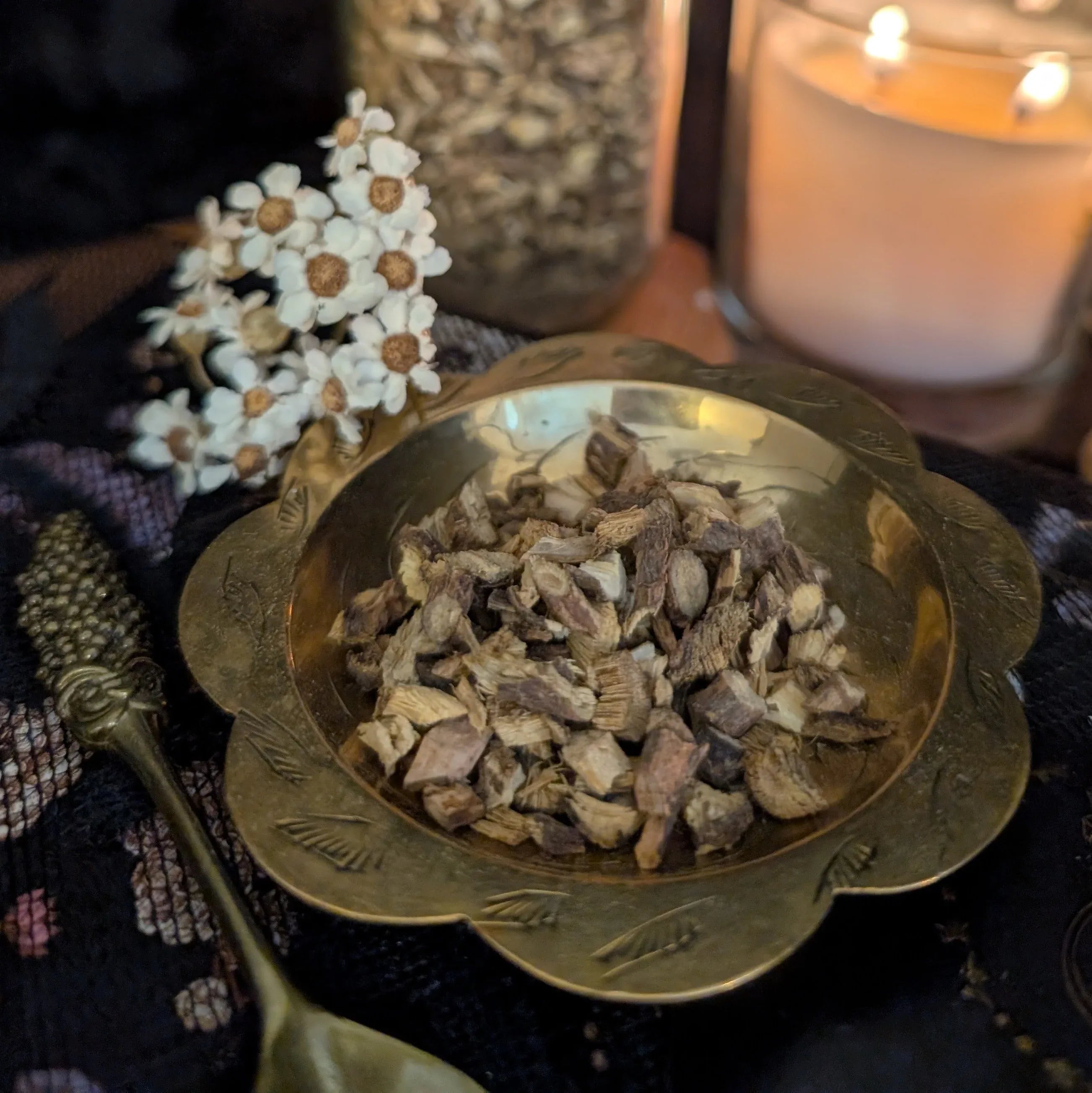 Brass bowl with dried liquorice on a textured surface with a candle in the background