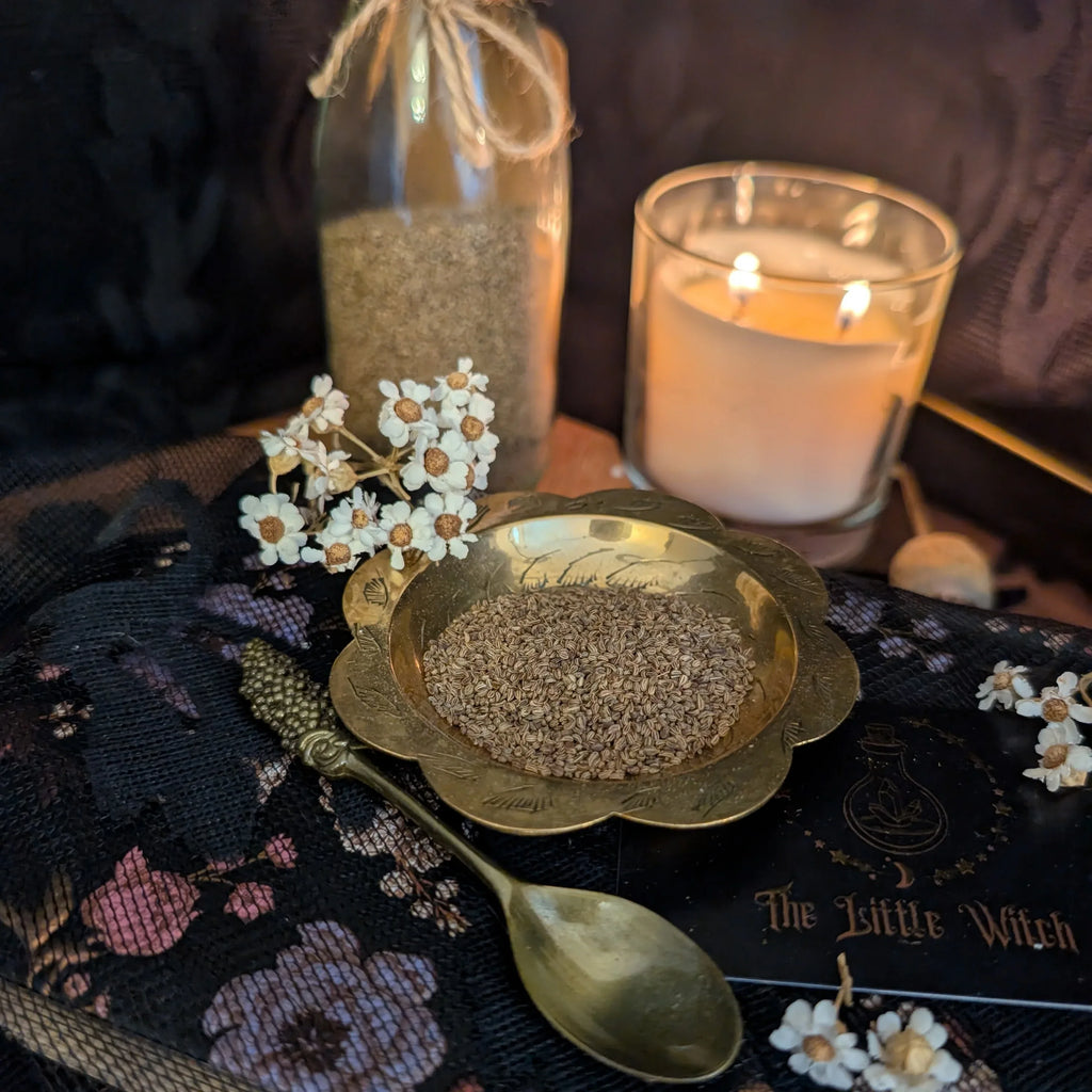 Lovage herbs in a gold dish with a lit candle and decorative spoon on a dark fabric background.