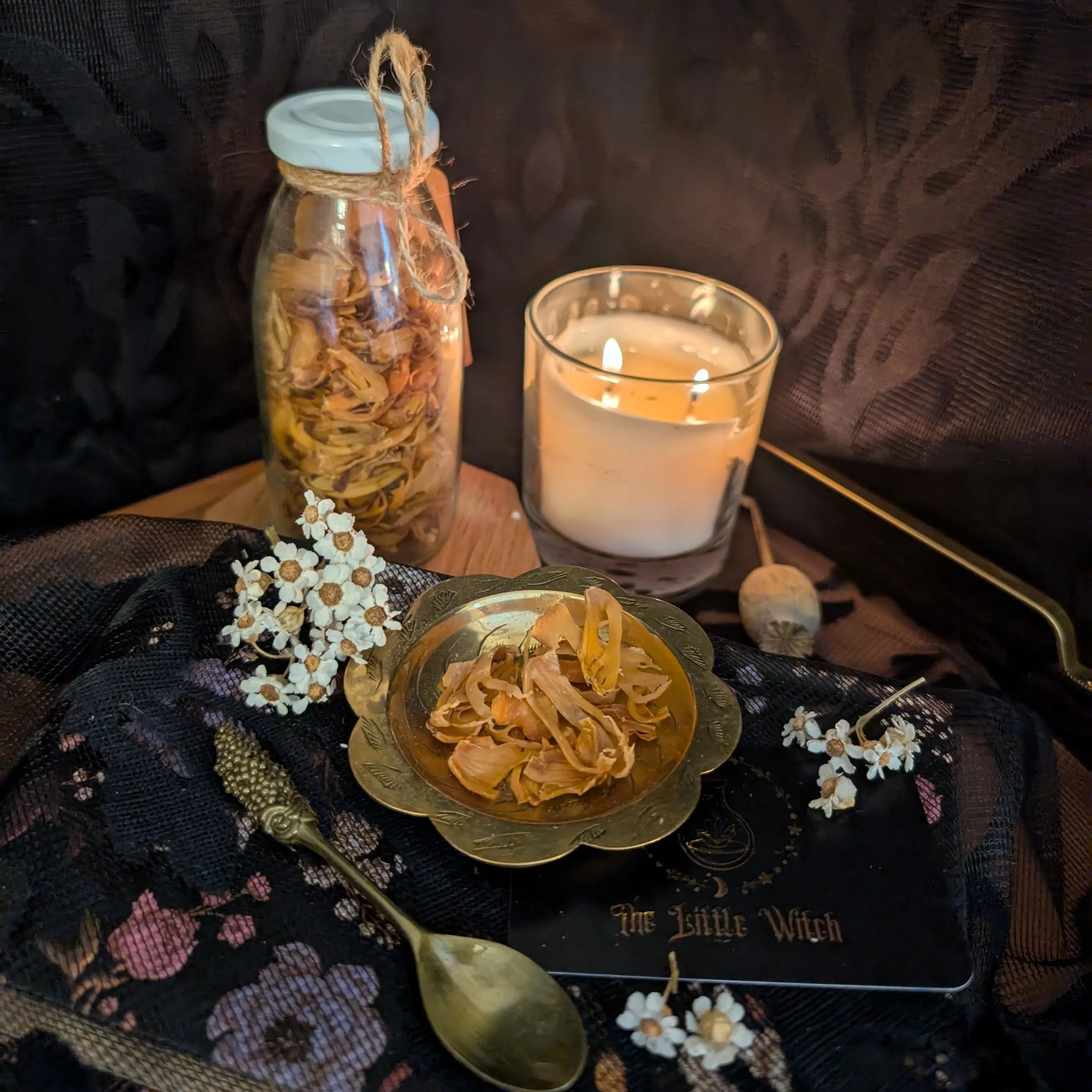 Gold dish containing dried Mace Blades with jar, candle, and decorative items on a dark surface.