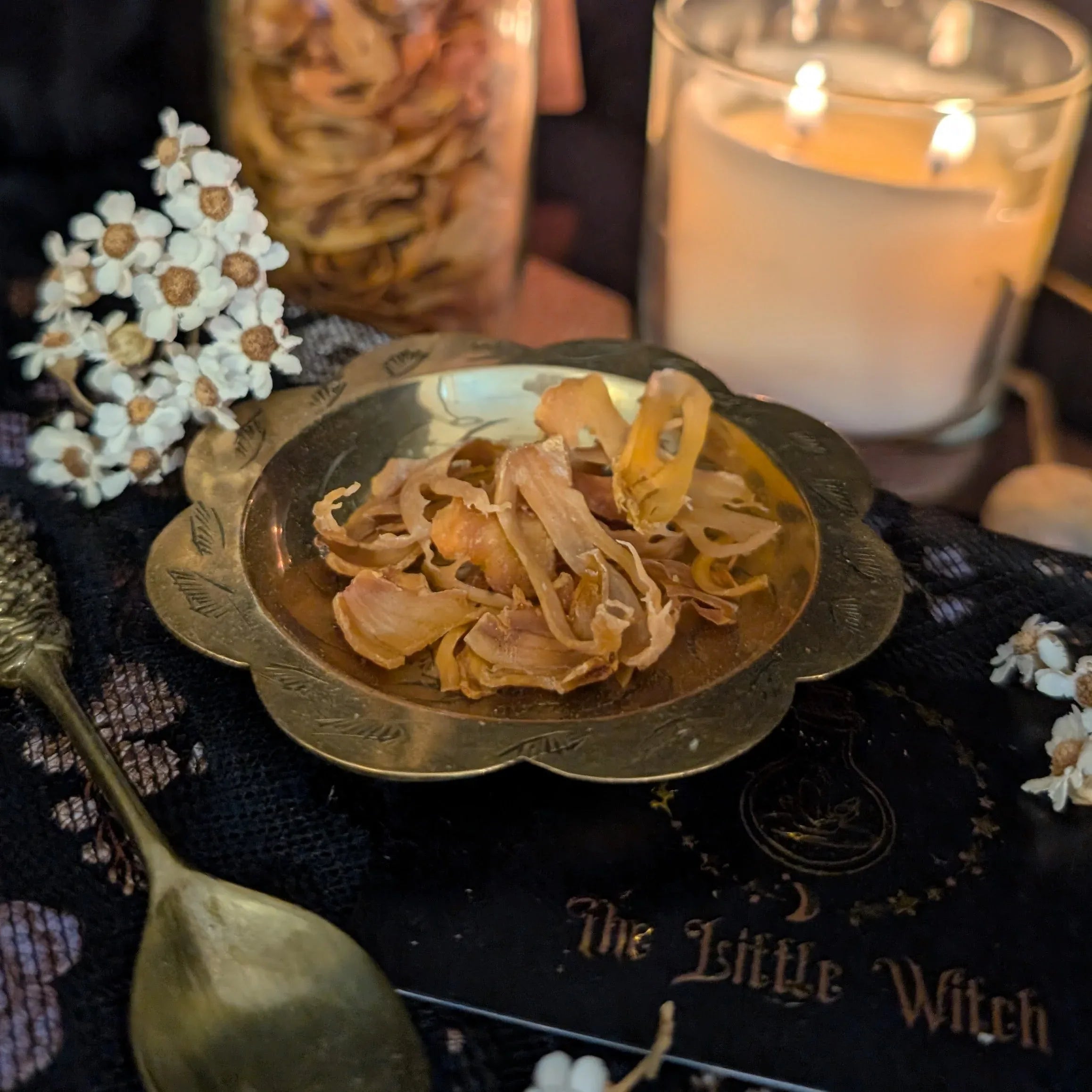 Dried Mace on a gold dish with a candle and decorative elements on a dark surface.