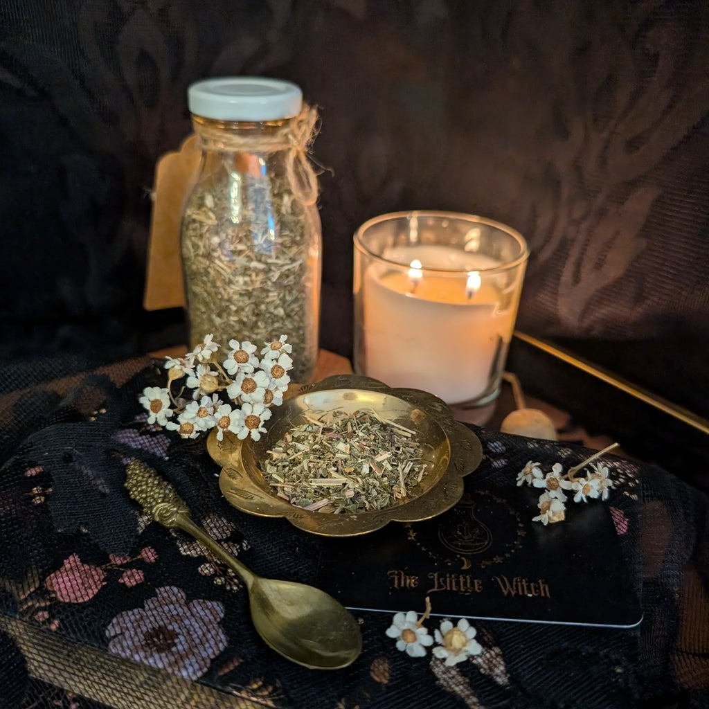 Dried Marjoram in a jar and on a plate with a lit candle and flowers on a dark surface.